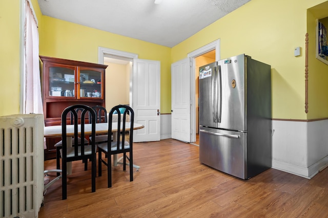 kitchen with baseboards, light wood finished floors, radiator heating unit, and freestanding refrigerator