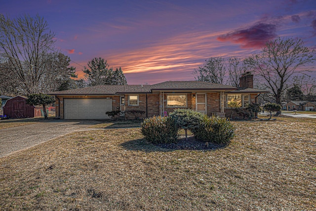 ranch-style home featuring brick siding, a chimney, a storage shed, a garage, and driveway