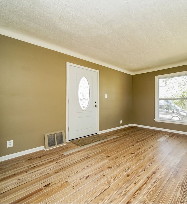 entrance foyer with light wood-type flooring, baseboards, a textured ceiling, and visible vents