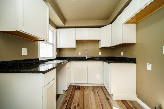 kitchen featuring a sink, white cabinetry, dark stone countertops, and light wood finished floors