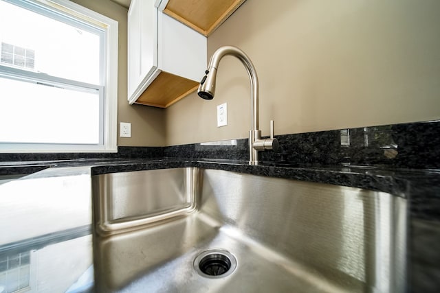 interior details featuring visible vents, white cabinetry, dark stone counters, and a sink