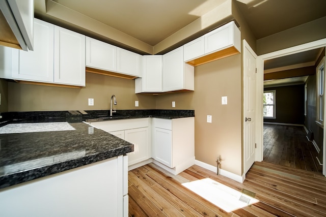 kitchen featuring a sink, white cabinetry, dark stone counters, light wood finished floors, and baseboards