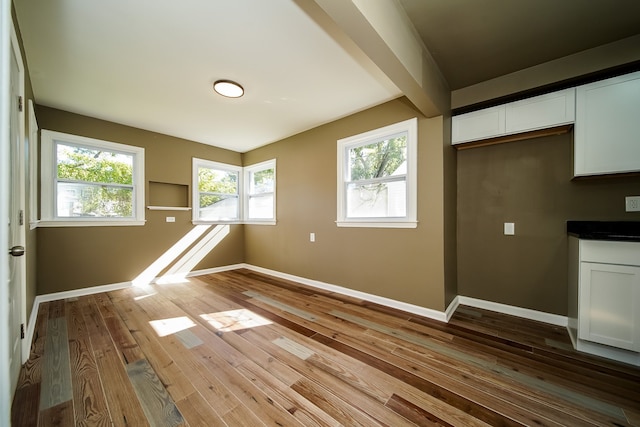 empty room featuring beamed ceiling, baseboards, and wood-type flooring