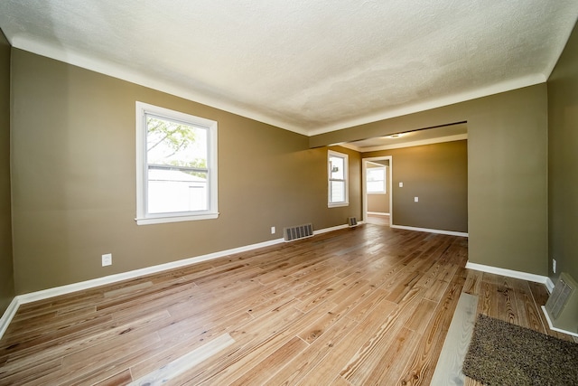 empty room featuring a wealth of natural light, visible vents, baseboards, and light wood-style floors