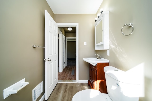 half bathroom featuring vanity, wood finished floors, visible vents, baseboards, and toilet