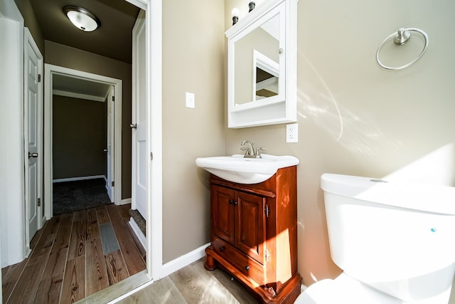 half bath featuring toilet, vanity, baseboards, and wood finished floors