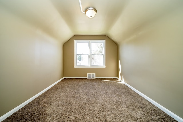 additional living space with vaulted ceiling, baseboards, visible vents, and dark carpet