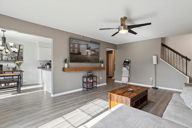 living area featuring stairway, baseboards, wood finished floors, and ceiling fan with notable chandelier