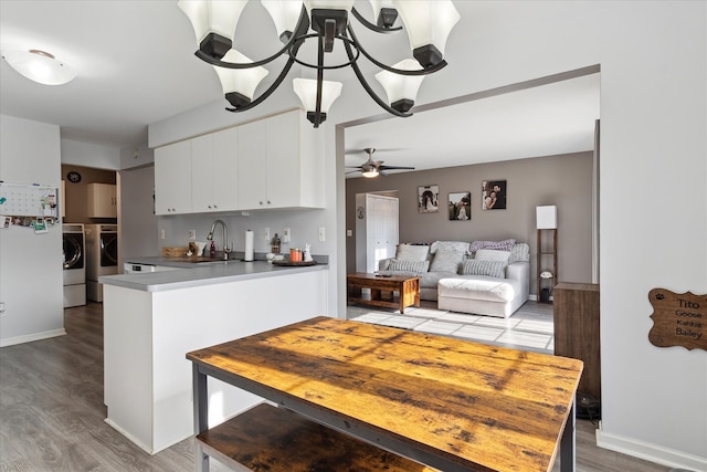 kitchen featuring wood finished floors, a peninsula, separate washer and dryer, a sink, and white cabinets