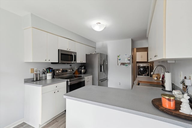 kitchen featuring a sink, washer / clothes dryer, white cabinetry, appliances with stainless steel finishes, and a peninsula