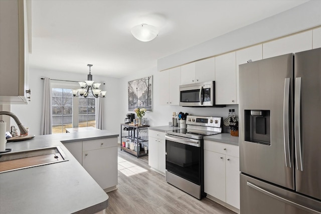 kitchen featuring a peninsula, light wood-style flooring, a sink, stainless steel appliances, and white cabinets