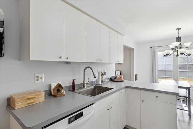 kitchen with a sink, a peninsula, white dishwasher, and white cabinetry