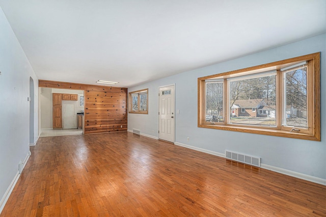 unfurnished living room with visible vents, arched walkways, baseboards, and wood finished floors