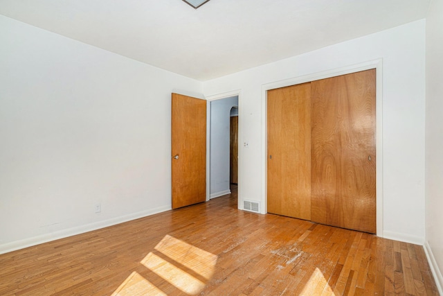 unfurnished bedroom with a closet, baseboards, visible vents, and wood-type flooring