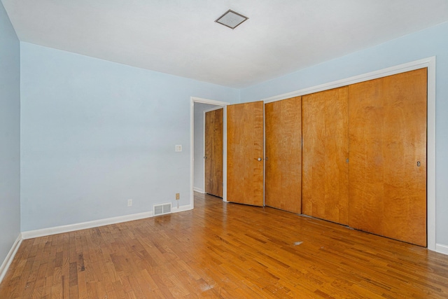 unfurnished bedroom featuring visible vents, wood-type flooring, baseboards, and a closet