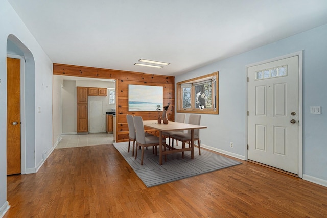 dining area featuring light wood-type flooring, arched walkways, and baseboards