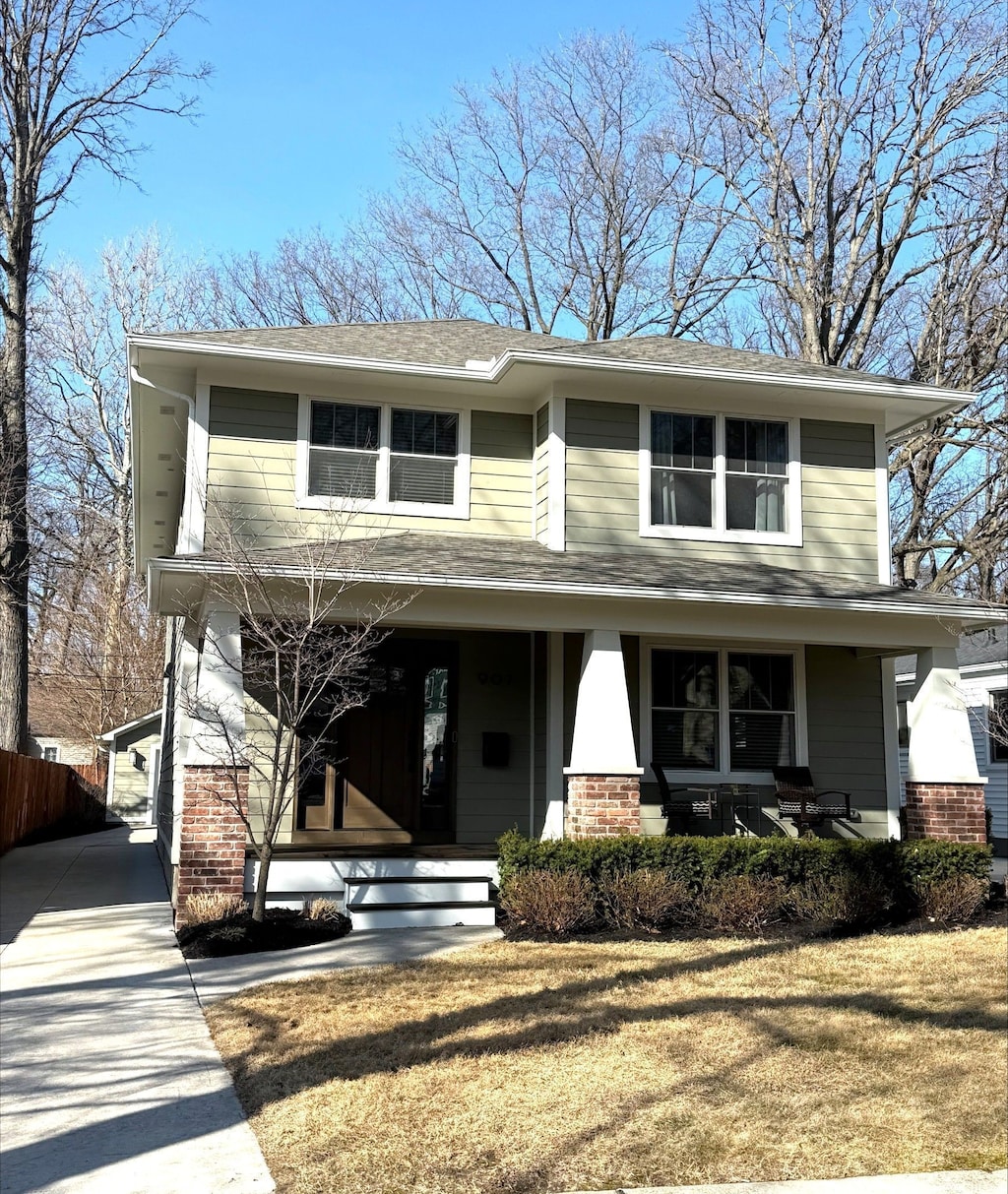 view of front of house featuring brick siding, covered porch, concrete driveway, and fence