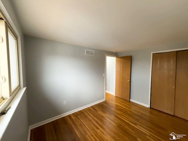 unfurnished bedroom featuring visible vents, baseboards, a closet, and wood finished floors