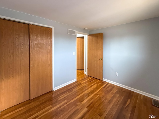 unfurnished bedroom featuring wood finished floors, visible vents, a closet, and baseboards