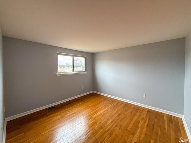 empty room with visible vents, wood-type flooring, and baseboards