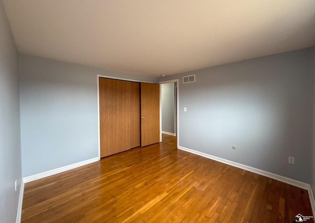 unfurnished bedroom featuring visible vents, wood-type flooring, baseboards, and a closet