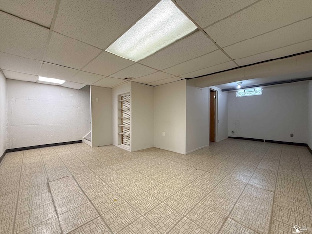 basement with a drop ceiling, stairs, and baseboards