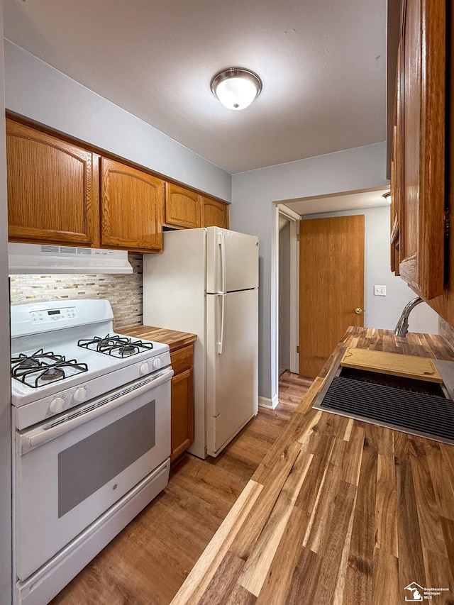 kitchen with under cabinet range hood, brown cabinets, light wood-style floors, white appliances, and a sink