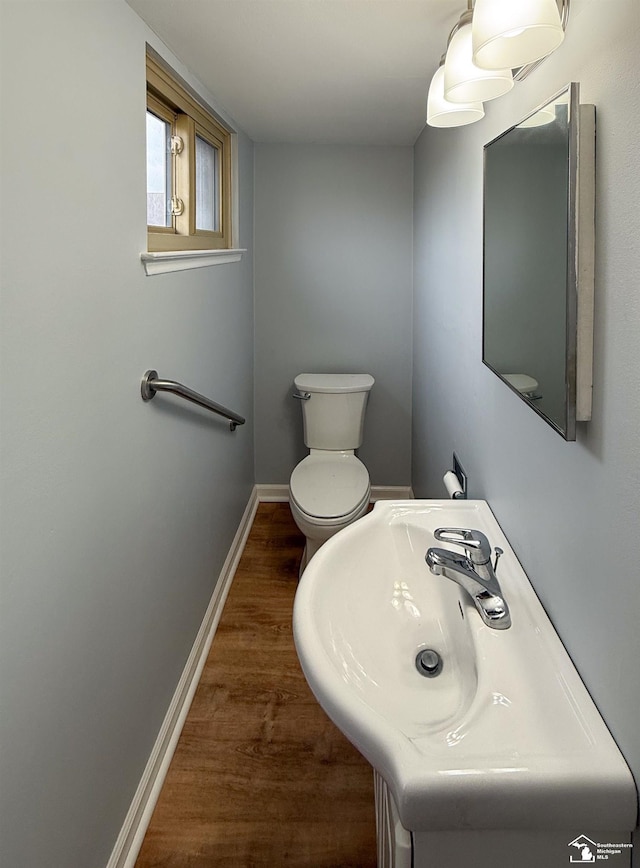 bathroom with toilet, wood finished floors, baseboards, and a sink