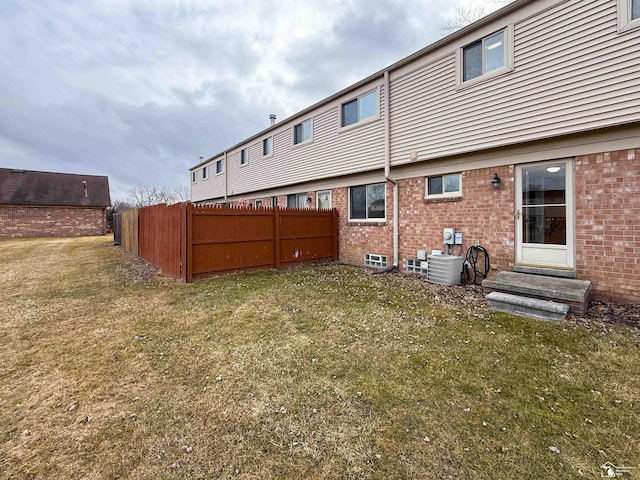 back of property featuring brick siding, a lawn, and fence