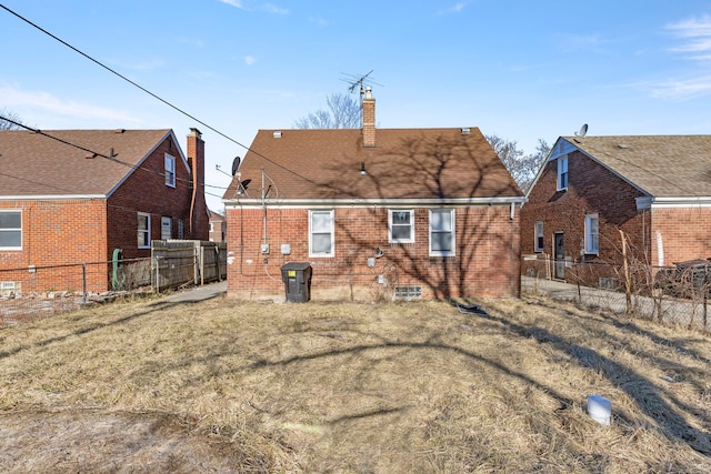 back of house featuring brick siding, a chimney, a yard, and fence