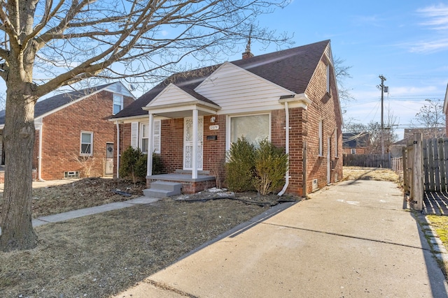 bungalow-style house featuring brick siding, a shingled roof, a chimney, and fence