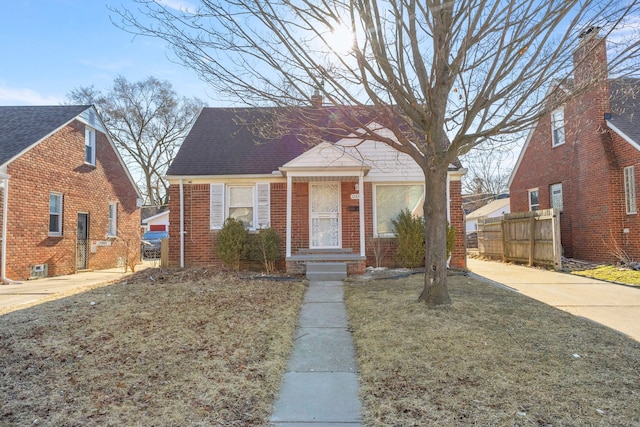 view of front of house featuring fence, brick siding, and roof with shingles