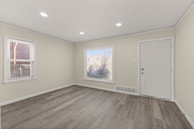 empty room with a wealth of natural light, visible vents, baseboards, and wood finished floors