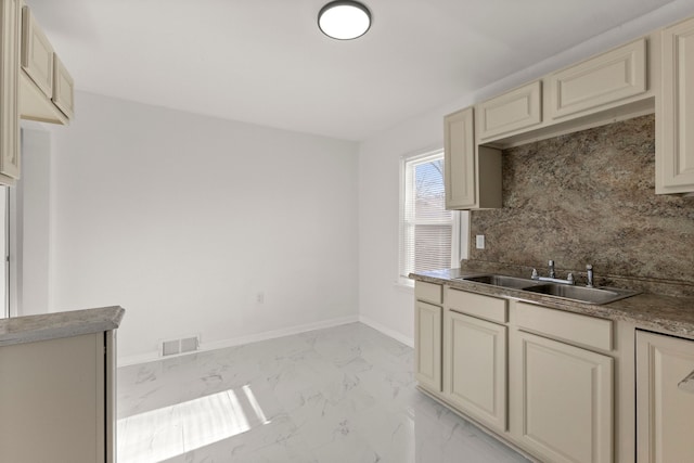 kitchen featuring visible vents, marble finish floor, a sink, cream cabinets, and baseboards