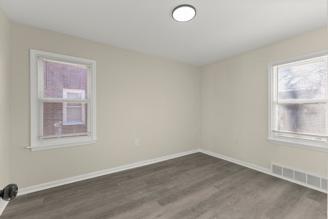 spare room with dark wood-style floors, visible vents, and baseboards