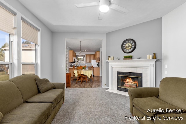 living room with a tiled fireplace, dark colored carpet, and ceiling fan