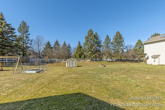 view of yard featuring a storage unit, a vegetable garden, an outdoor structure, and fence