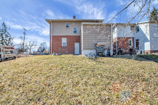 back of property featuring a yard, brick siding, and a chimney