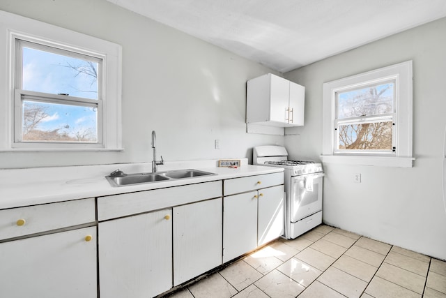 kitchen with light tile patterned floors, white range with gas cooktop, a sink, light countertops, and white cabinets