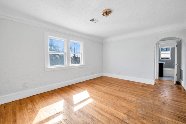 unfurnished room featuring visible vents, arched walkways, a textured ceiling, and hardwood / wood-style floors