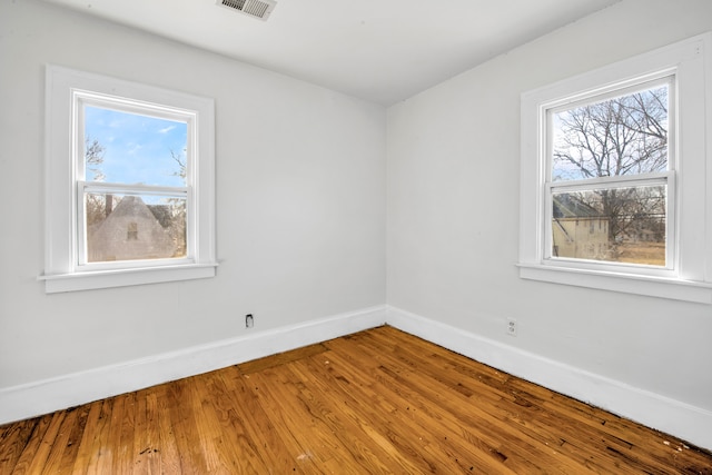 spare room with visible vents, a healthy amount of sunlight, baseboards, and wood-type flooring