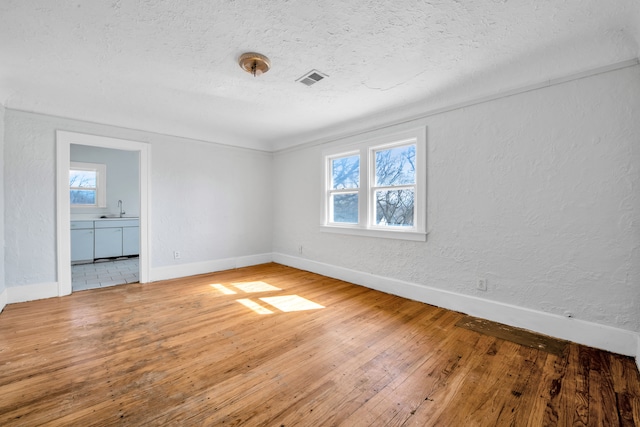 spare room featuring baseboards, visible vents, hardwood / wood-style flooring, a textured ceiling, and a textured wall