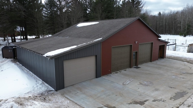 snow covered garage with a detached garage and a forest view