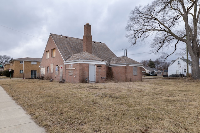 view of home's exterior with brick siding, a chimney, and a yard