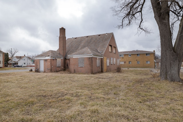 rear view of property featuring a yard, brick siding, and a chimney