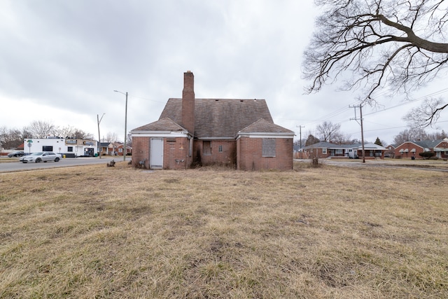 exterior space featuring a yard, brick siding, a chimney, and a shingled roof