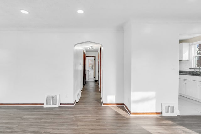 hallway featuring a sink, visible vents, arched walkways, and ornamental molding