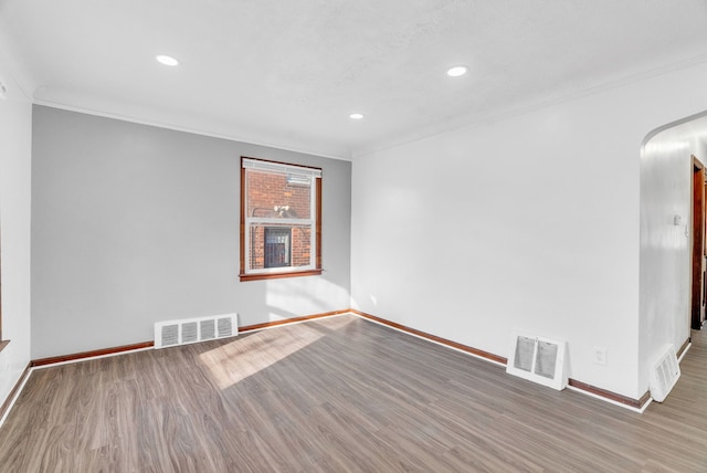 spare room featuring wood finished floors, crown molding, arched walkways, and visible vents