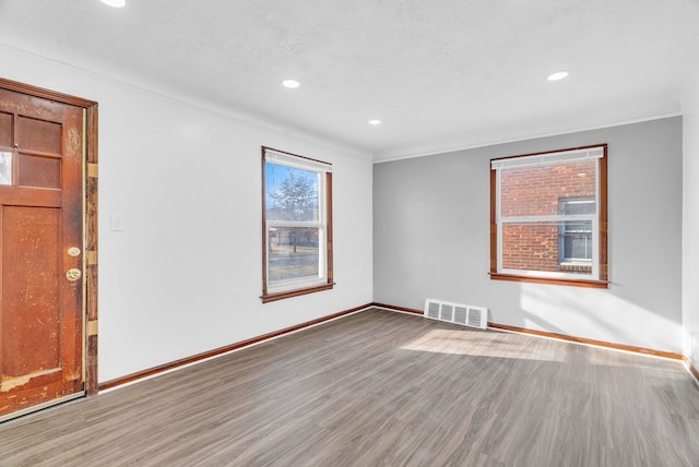 spare room with crown molding, wood finished floors, visible vents, and baseboards