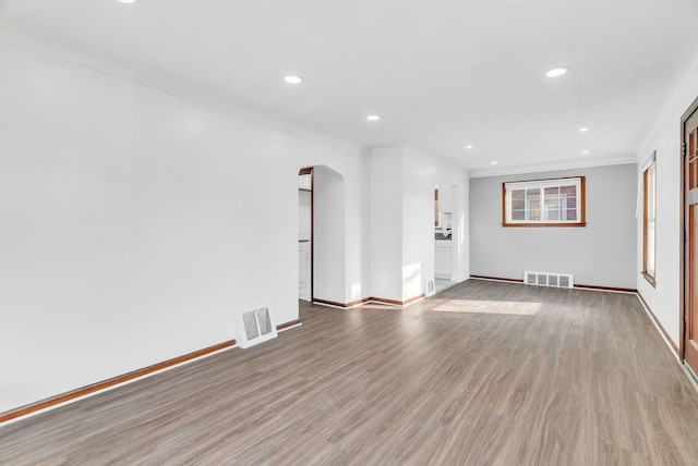 unfurnished living room with wood finished floors, arched walkways, visible vents, and baseboards